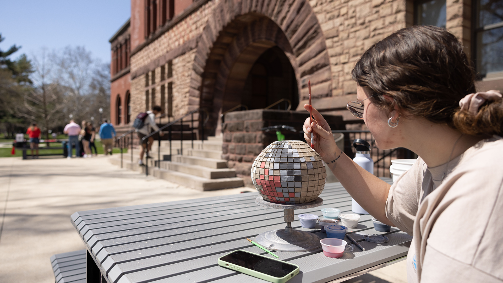 Individual sitting at a picnic table working on an art project with their cell phone lying on the table nearby