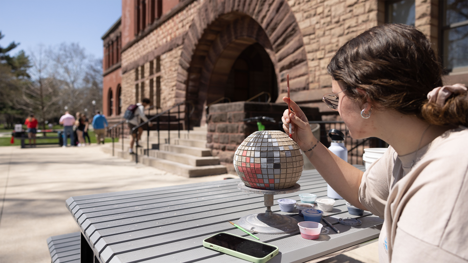 Individual sitting at a picnic table working on an art project with their cell phone lying on the table nearby